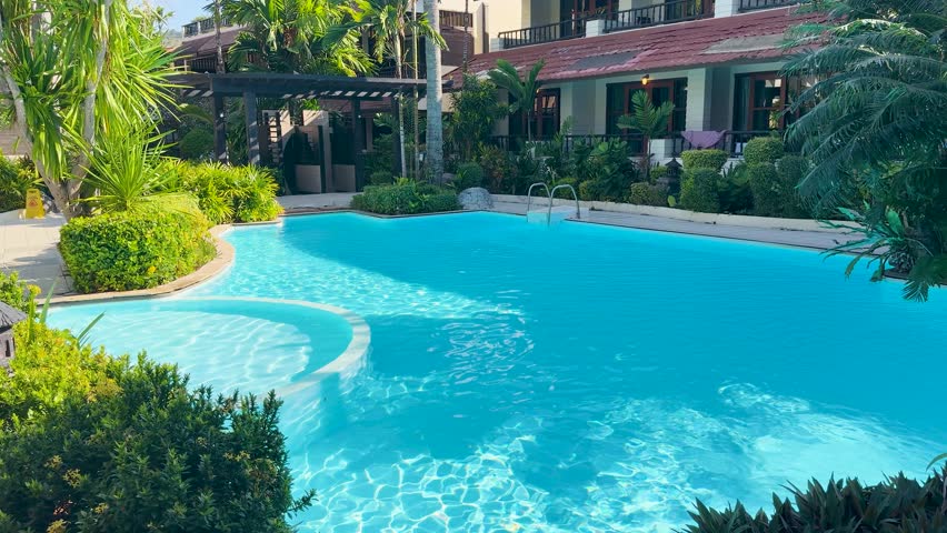 A wide shot of a bright turquoise swimming pool surrounded by lush tropical greenery