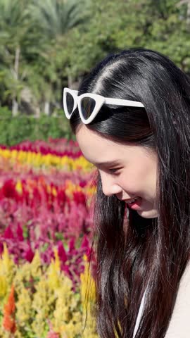 A happy woman walks through a sunny field of red and yellow flowers in profile