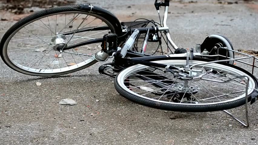 A bicycle lies fallen on the ground with its wheels up after an accident outdoors, surrounded by pavement and scattered debris.