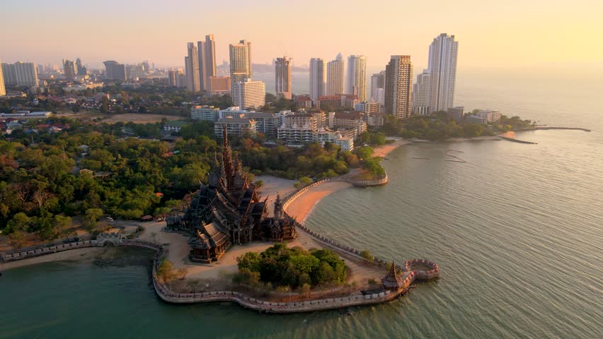 Marvel at the intricate wooden architecture of the Sanctuary of Truth in Pattaya, Thailand. This stunning structure glows beautifully at sunset, surrounded by the tranquil sea and city skyline.