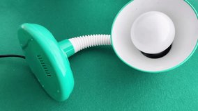 A hand uses a screwdriver to assemble or repair a green desk lamp with a flexible neck, showing a simple DIY process of maintaining or adjusting everyday lighting equipment in a workspace - Powered by Shutterstock - Get 15% off with code: PIKWIZARD15