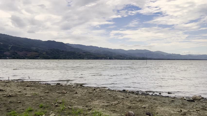 Shoreline With Mountains and Cloudy Sky