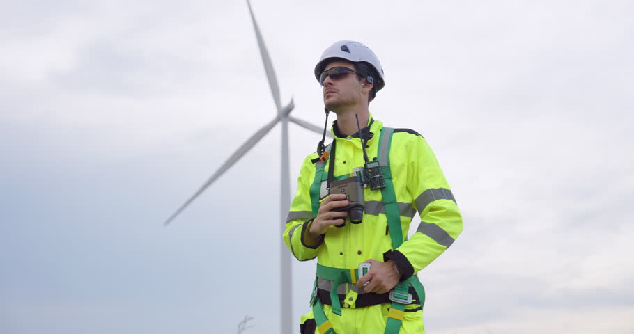 Engineer standing near wind turbine using walkie talkie, professional worker monitoring renewable power system, representing green innovation, sustainable technology, and safety in clean energy
