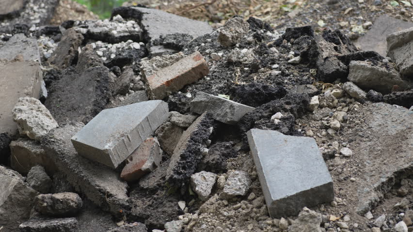 Pile of broken bricks and concrete slabs rests in residential courtyard. Rough textures and urban decay contrast quiet multi-story housing