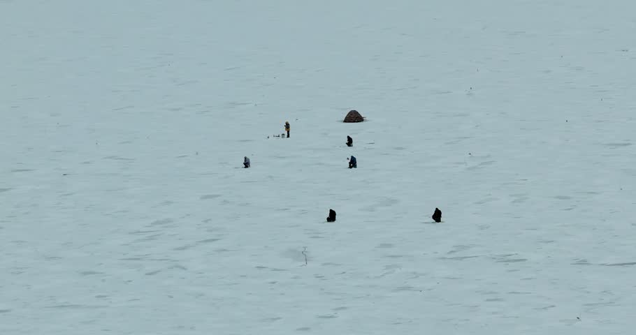 Drone orbit around ice fishermen on frozen lake winter aerial shot with people fishing on ice