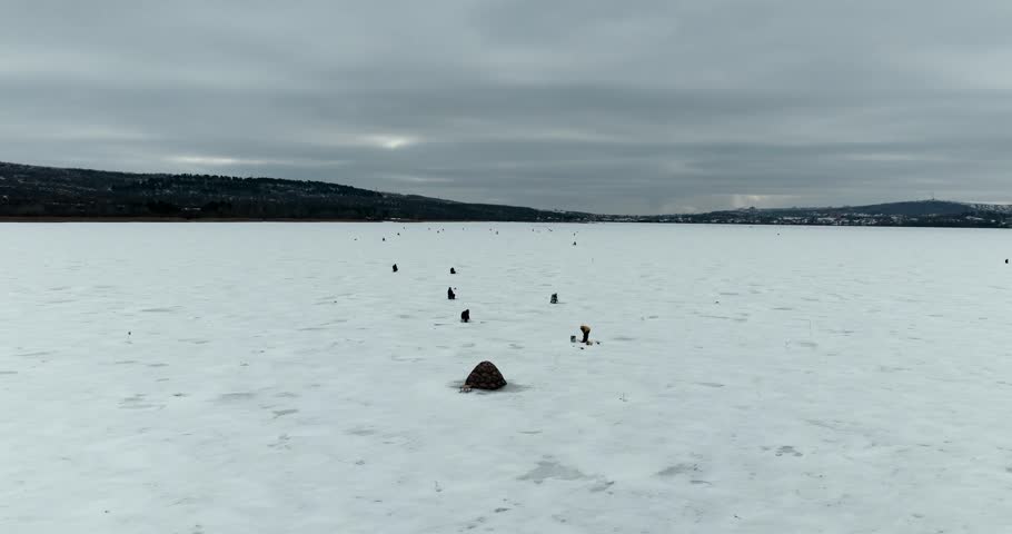 Drone orbit around ice fishermen with winter fishing tent on frozen lake aerial shot