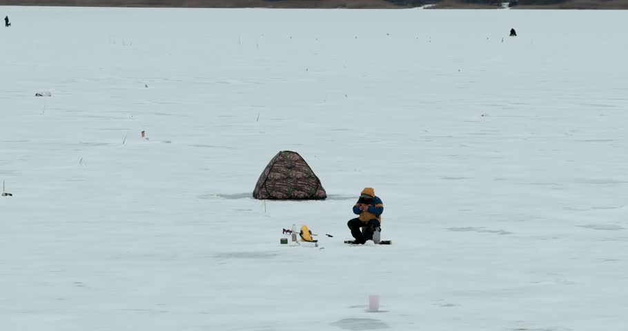 Drone orbit around ice fisherman and winter fishing tent on frozen lake close aerial shot