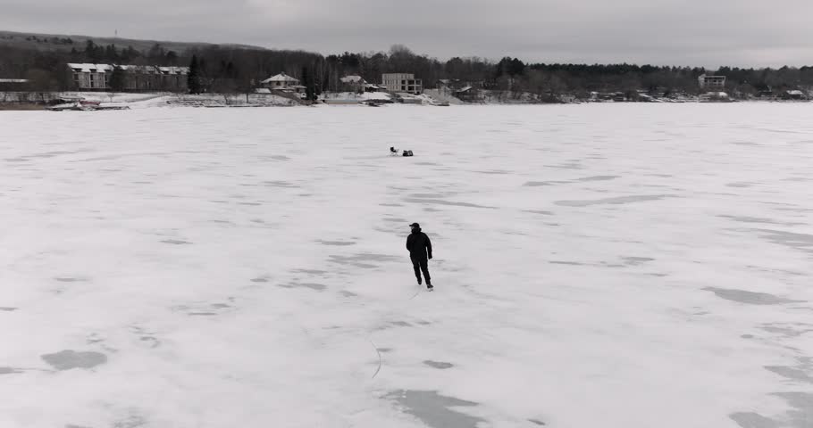 Aerial drone view of man skating backward doing turns and falling on frozen lake winter sport action