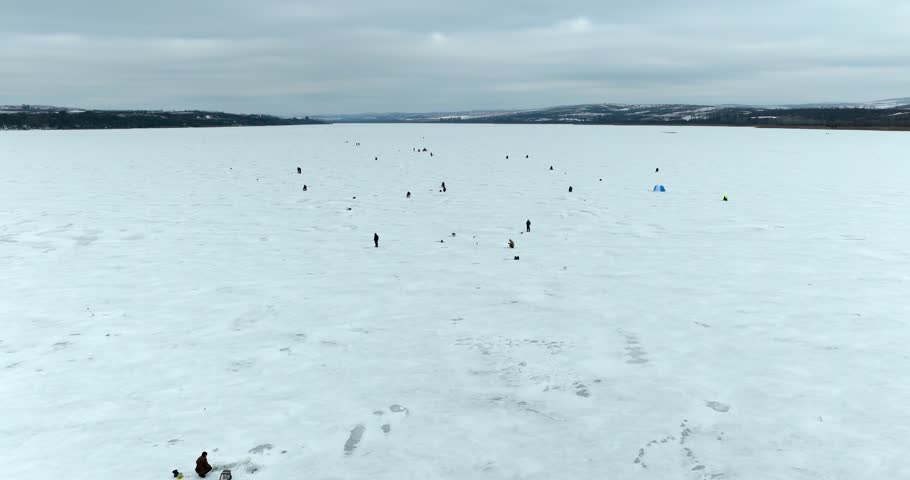 Aerial orbit around ice fishermen on frozen lake winter drone shot over people fishing on ice