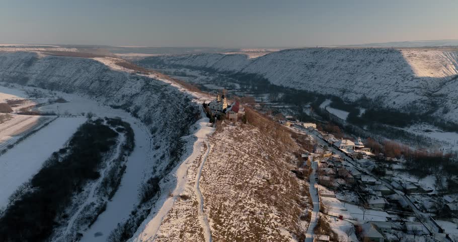 Aerial drone approach and flythrough between golden crosses toward Orheiul Vechi Orthodox monastery on snowy cliff in winter