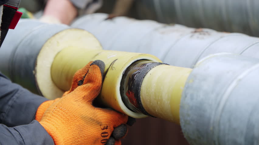 Technical repair process shows workers stabilizing insulated pipes. Rough materials and winter conditions amplify industrial realism