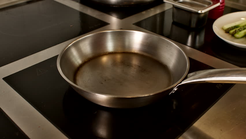 Close-up of olive oil shimmering in a hot metal pan on an induction stovetop in a generic kitchen. Professional start to a sautéing or frying culinary process
