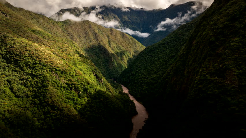 Drone flight through lush green valley in Andes mountains near Aguas Calientes, with clouds over the peaks, Peru. Aerial forward, hyperlapse time-lapse