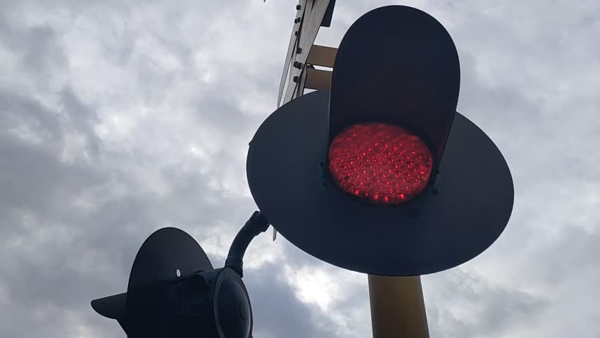 Low angle video of railway crossing signal lights against a dramatic cloudy sky. Concept for transportation safety, railroad infrastructure, warning signs, and travel journey.