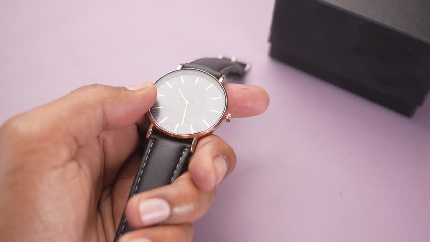 Close up hand holding wristwatch, checking time on analog watch with black dial and leather strap