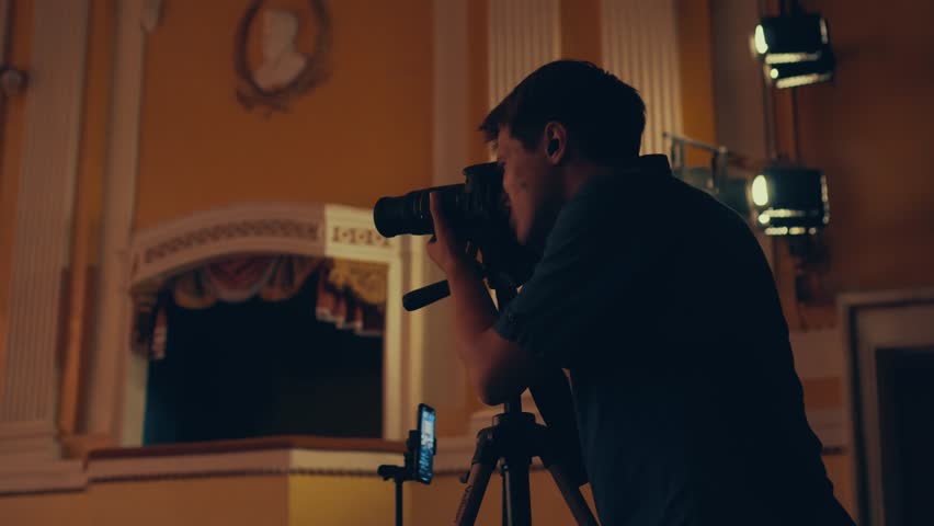 A photographer at a concert looks through the viewfinder and takes a photo. A young male photographer holds a camera taking pictures. Reportage shooting of the concert.