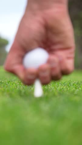 A person is holding a golf ball and putting it on a golf tee. Concept of focus and concentration, as the person is preparing to take a shot