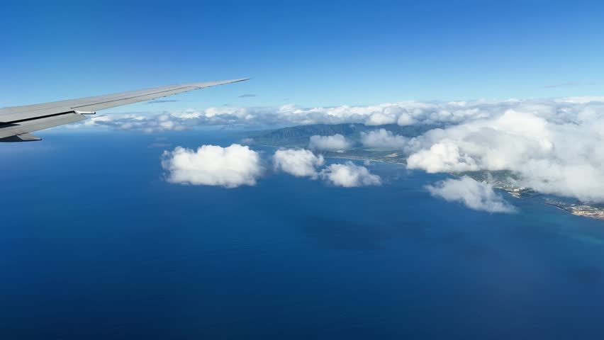View from airplane window showing Oahu coastline, blue ocean, clouds, and wing