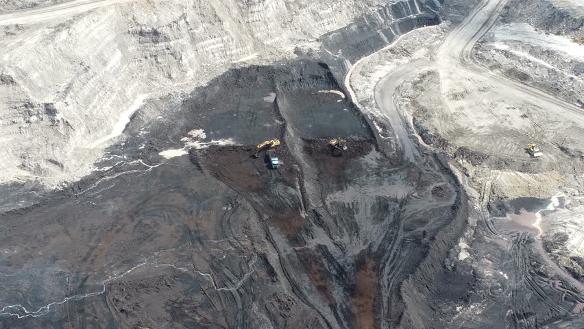 An aerial view of a blackened coal mine pit filled with coal, as well as the loading and unloading of trucks