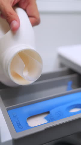 Close up of a hand pouring liquid fabric softener into the dispenser drawer of a washing machine. Laundry day and housekeeping concept. Vertical Shot.