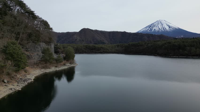 Scenic view of Mount Fuji with calm lake and a road visible on the left side. Peaceful Japanese landscape combining nature travel and quiet human presence