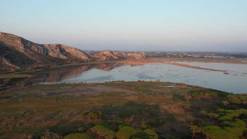 Panoramic wetland lagoon with calm reflections and rocky hills at sunset