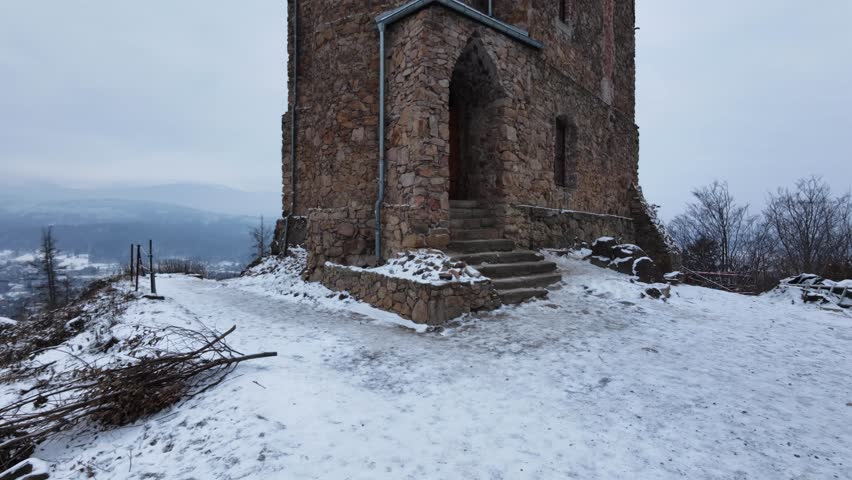 A historic stone tower standing tall in a snowy landscape. The cold weather and cloudy sky give a dramatic and timeless historical atmosphere.