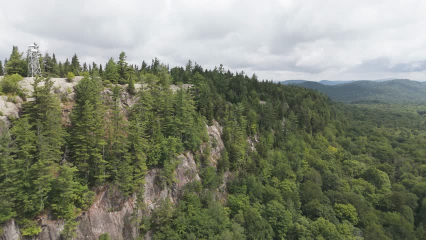 Aerial summer view of a mountain fire tower atop Bald Mountain near Old Forge in the Adirondacks during clear daylight and peaceful conditions.