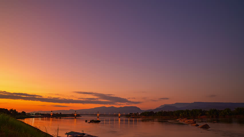 Time lapse A dreamlike sunset casting golden light over the Mekong River and the Fifth Thai–Lao Friendship Bridge in Bueng Kan, creating a surreal and peaceful atmosphere. colorful Reflection
