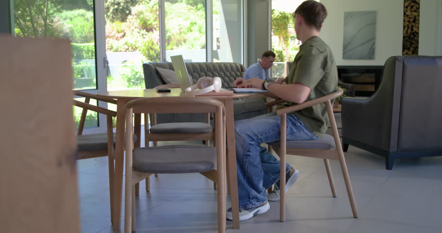 Family teenage son at home, father rising, pointing at laptop notes helping study while son writing. Youth, tutoring, guidance, collaboration, homework, parent, computer