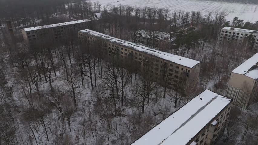 Cinematic drone footage of an abandoned Soviet-era barracks complex near Leipzig, Germany. Snow-covered buildings lie scattered through a quiet forest, creating a moody winter atmosphere.