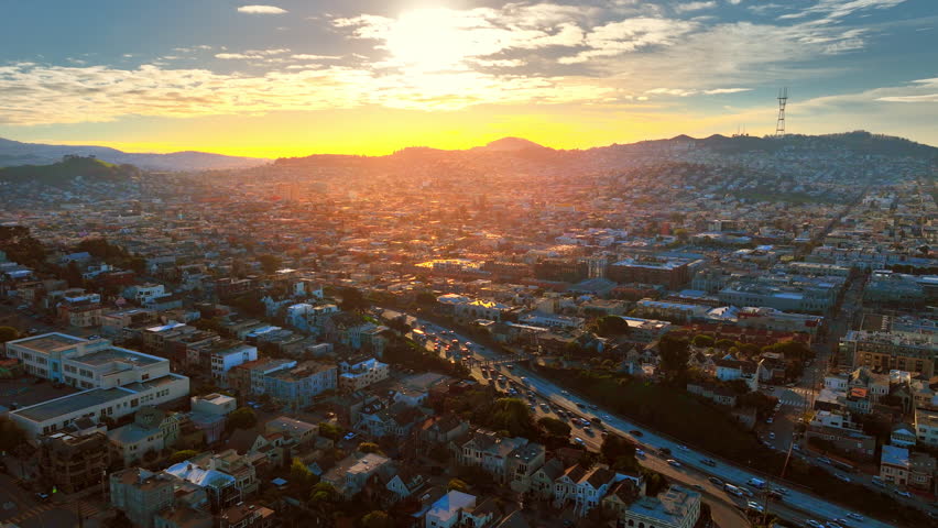 Residential area with houses in downtown San Francisco at sunset in bright rays. Television tower on Twin Peaks hills. Aerial view. Highway with cars.