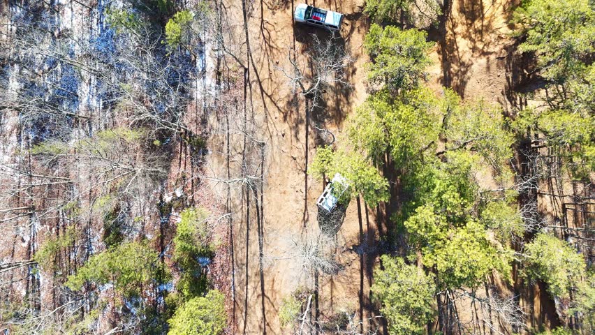 Police car on dirt road in wooded area from above