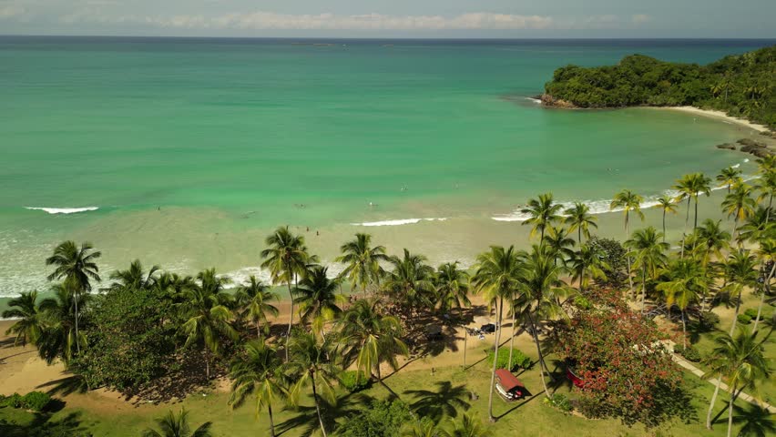 Wide aerial panorama of Bonita Beach with turquoise ocean, soft sand, palm trees, and gentle waves under bright tropical sunlight. Perfect for travel and tourism promotion.