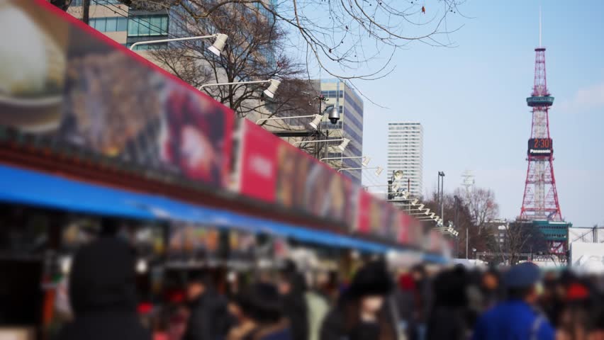 Blurred crowd at Sapporo Snow Festival food stalls with TV Tower background abstract copy space