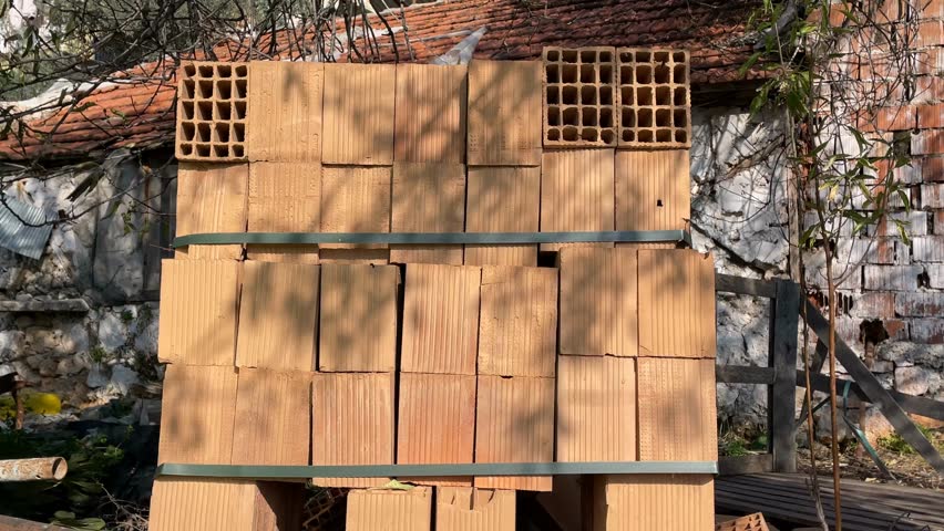 Stack of clay bricks against rustic building background with shadows from nearby foliage video