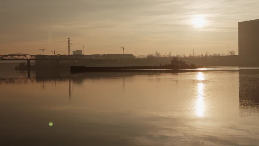 Industrial River Landscape with Barge Floating at Sunset, Cargo Ship Navigating Waterway near Bridge and Cranes, Golden Hour over City Port, Logistics and Maritime Transport on Calm River, Industrial Barge Moving Goods during Sunrise, Urban Ship Infrastructure