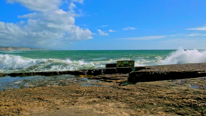 Large ocean waves crash about the  pier. Slow motion - ocean waves splashes. Beautiful sea with crashing waves about wharf on summer sunny day.  Sea water is  crashing on dock creating huge splashes