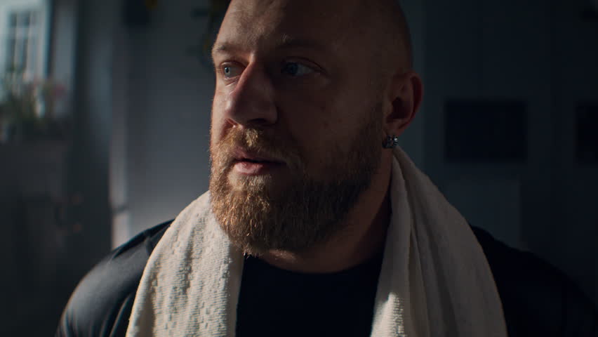Bearded sportsman with sweaty face and white towel on neck in gym closeup. Mature man athlete stands resting at active workout in sports center. Bodybuilding