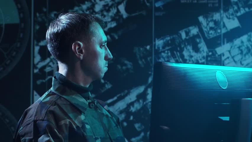 Soldier in a dimly lit military control room, intensely focused on multiple computer screens displaying crucial operational drone data.