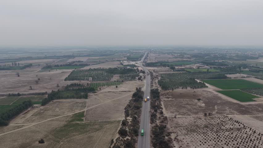 Aerial view of a highway with vehicles and agricultural fields on both sides under a cloudy sky in the distance