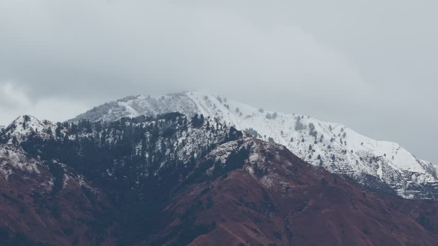 Aerial view of a Snow capped mountain peaks rising majestically against a cloudy sky with hints of rocky terrain visible below 4k footage 