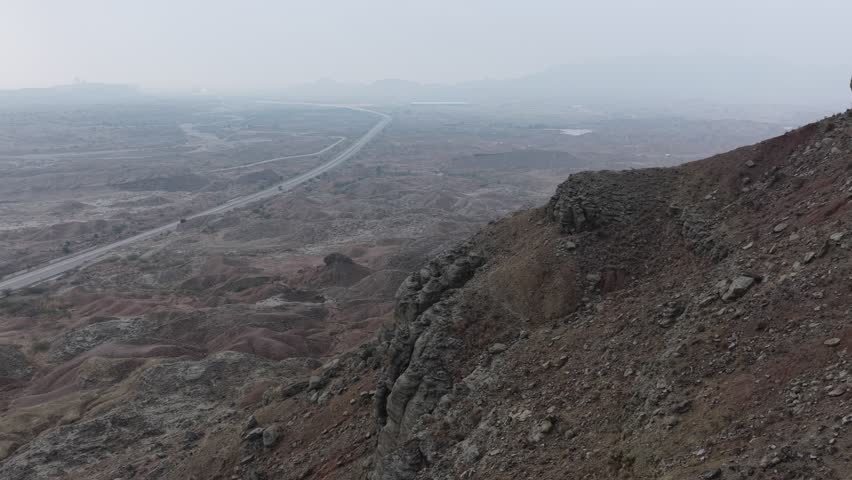 Aerial view of a winding road cutting through a barren landscape with patches of dry earth and sparse vegetation 4k footage