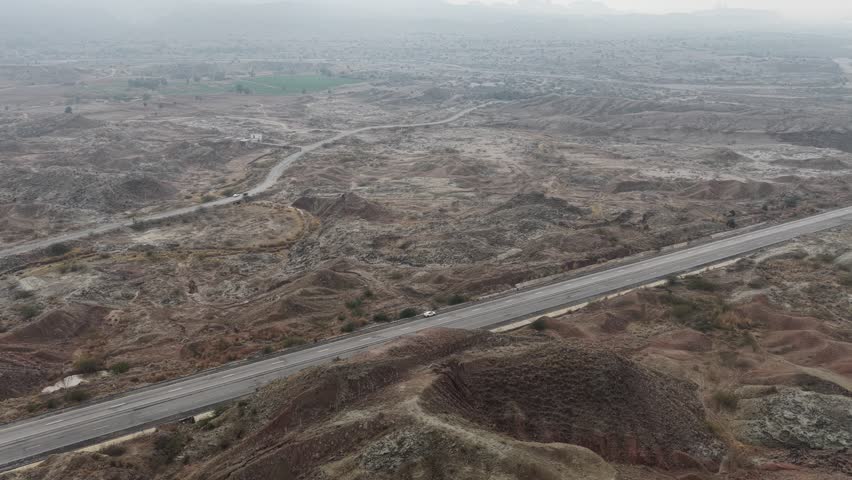 Aerial view of a winding road cutting through a barren landscape with patches of dry earth and sparse vegetation 4k footage