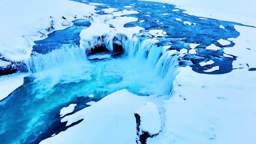 Aerial view of nearly frozen rivers in remote Iceland, with icy waterfalls cascading through rugged northern landscapes, snow-dusted terrain, and dramatic natural formations, capturing serene Arctic beauty and pristine wilderness in winter.