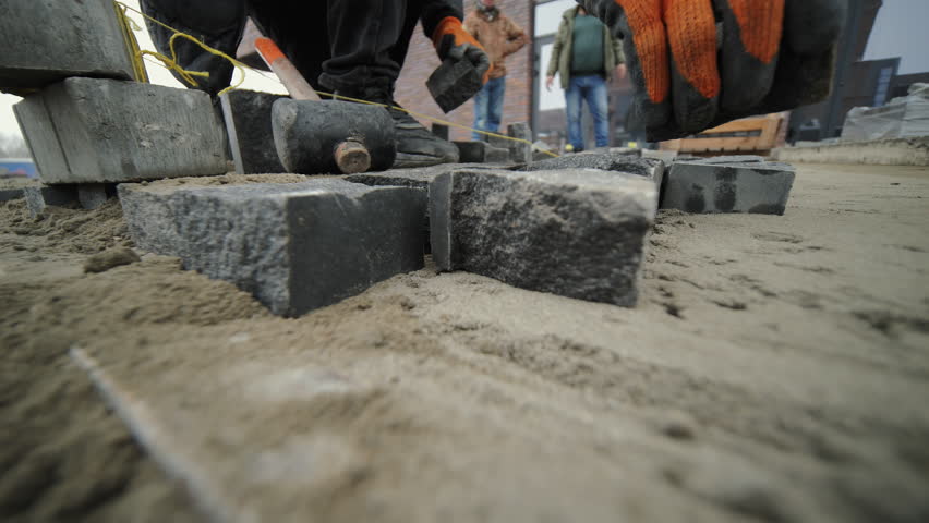 Aligning granite paving blocks on sand base during walkway construction
