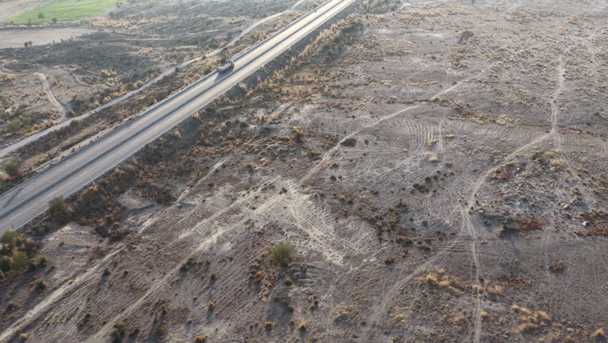 Aerial view of a dry landscape featuring cracked earth and sparse vegetation with railway tracks in the distance