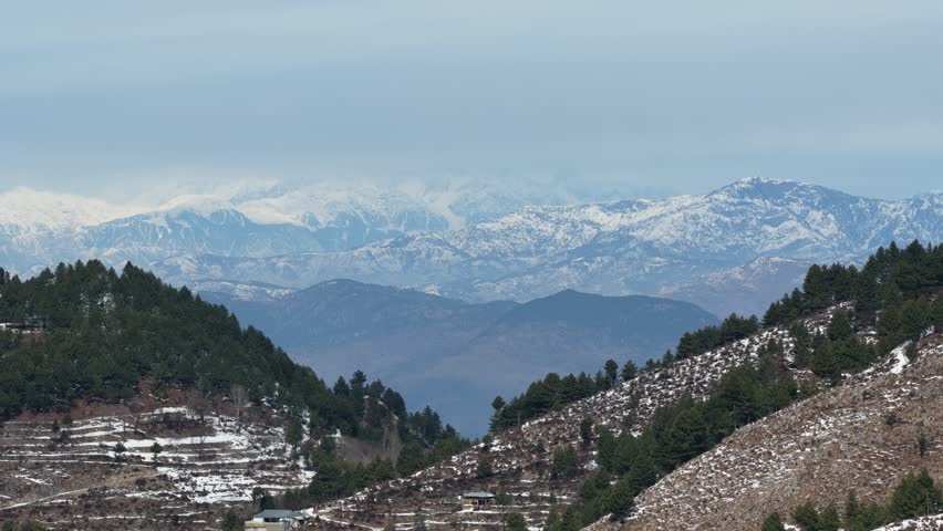 Aerial view of Snow capped mountains rise majestically in the distance surrounded by rocky terrain and patches of green vegetation