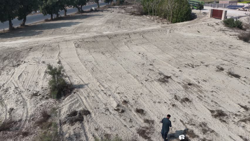 Aerial view drone shot of a Empty landscape with patches of dirt and sparse vegetation under a clear sky and distant structures on the horizon