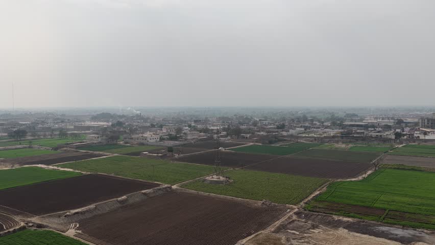Aerial view of agricultural fields with varying shades of green and brown crops alongside scattered buildings and roads